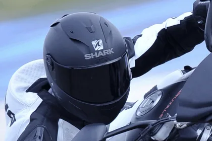Motard en combinaison sur sa moto, gros plan sur un casque intégral noir mat Shark vu de profil