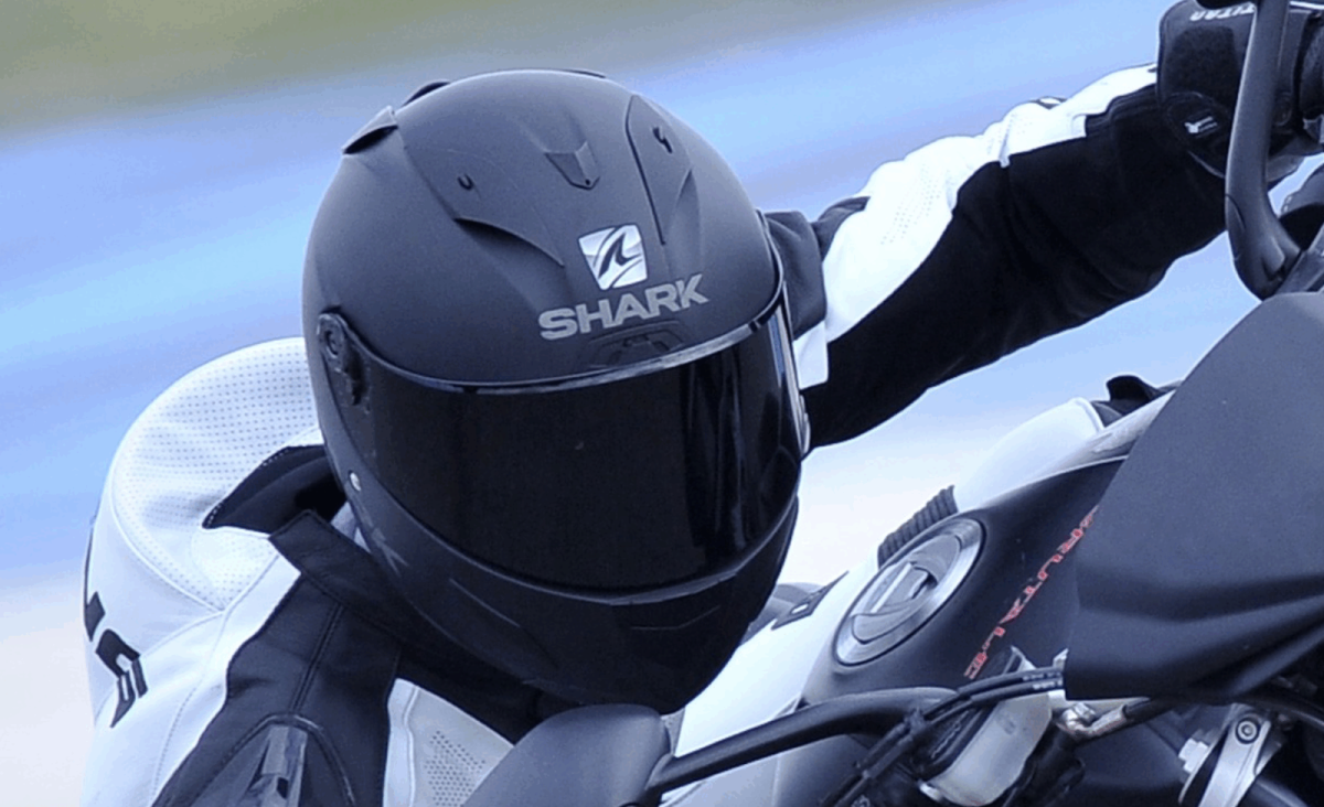 Motard en combinaison sur sa moto, gros plan sur un casque intégral noir mat Shark vu de profil